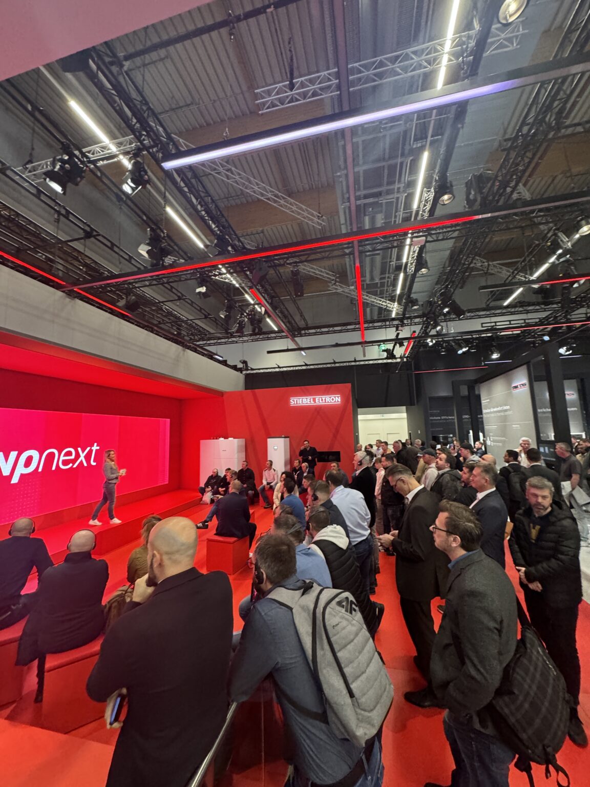 Dr. Ines Marbach moderiert an einem roten Messestand vor Publikum
